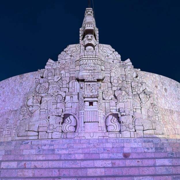 Decorative stone structure with intricate carvings against a dark blue sky in the Yucatan Peninsula.